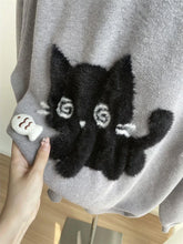 Load image into Gallery viewer, Gray sweater with a black cat applique held by a hand on a wooden surface. Mischief Meow Cozy Cat Sweater - Details- JBCoolCats