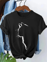 Load image into Gallery viewer, Black t-shirt with a white cat silhouette design, hanging on a wooden hanger with jeans in the background. Chic Silhouette Cat Tee - Clothing - JBCoolCats